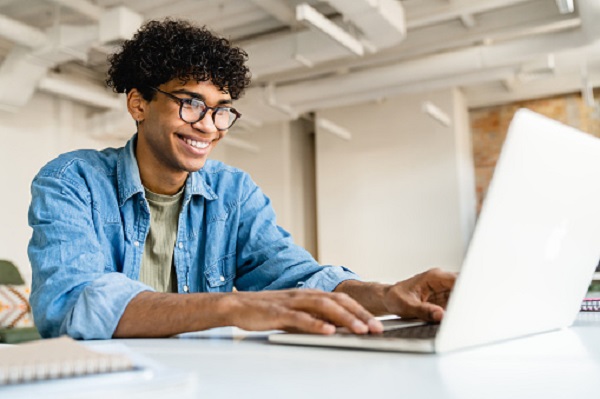 Happy smiling afro businessman using laptop at the desk in office Concours de la Fonction Publique répartition des centres d’écrit